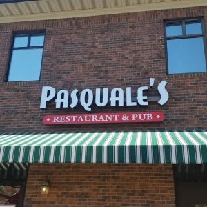 Channel letter sign on raceway that says "Pasquale's" installed on brick wall above awning.