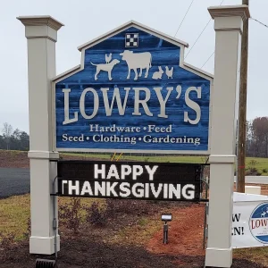A wood sign installed on posts for a hardware store that also has an electronic message board on it.